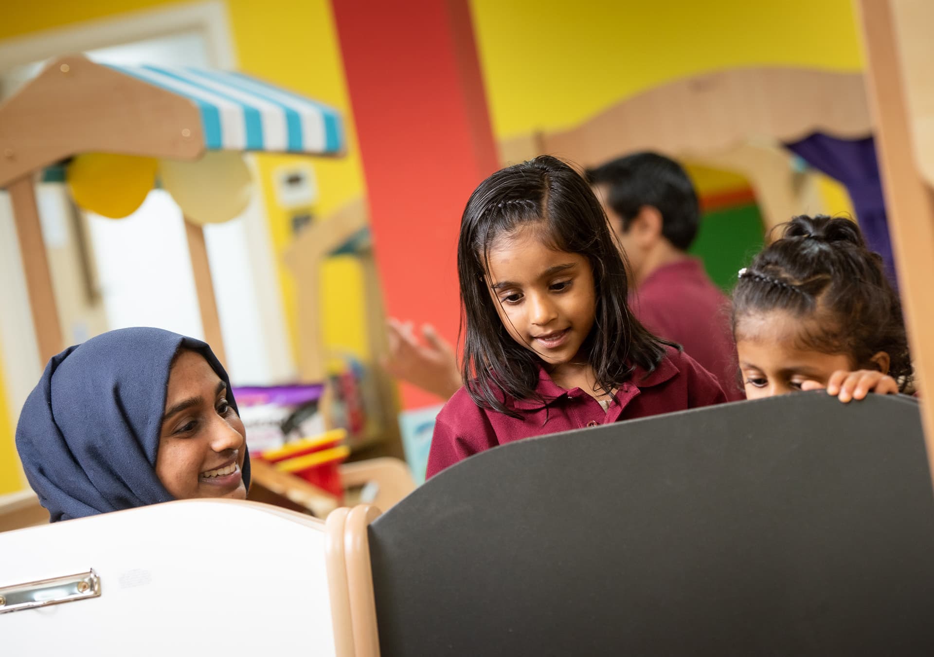 Two girls and a staff member playing with a chalkboard easel