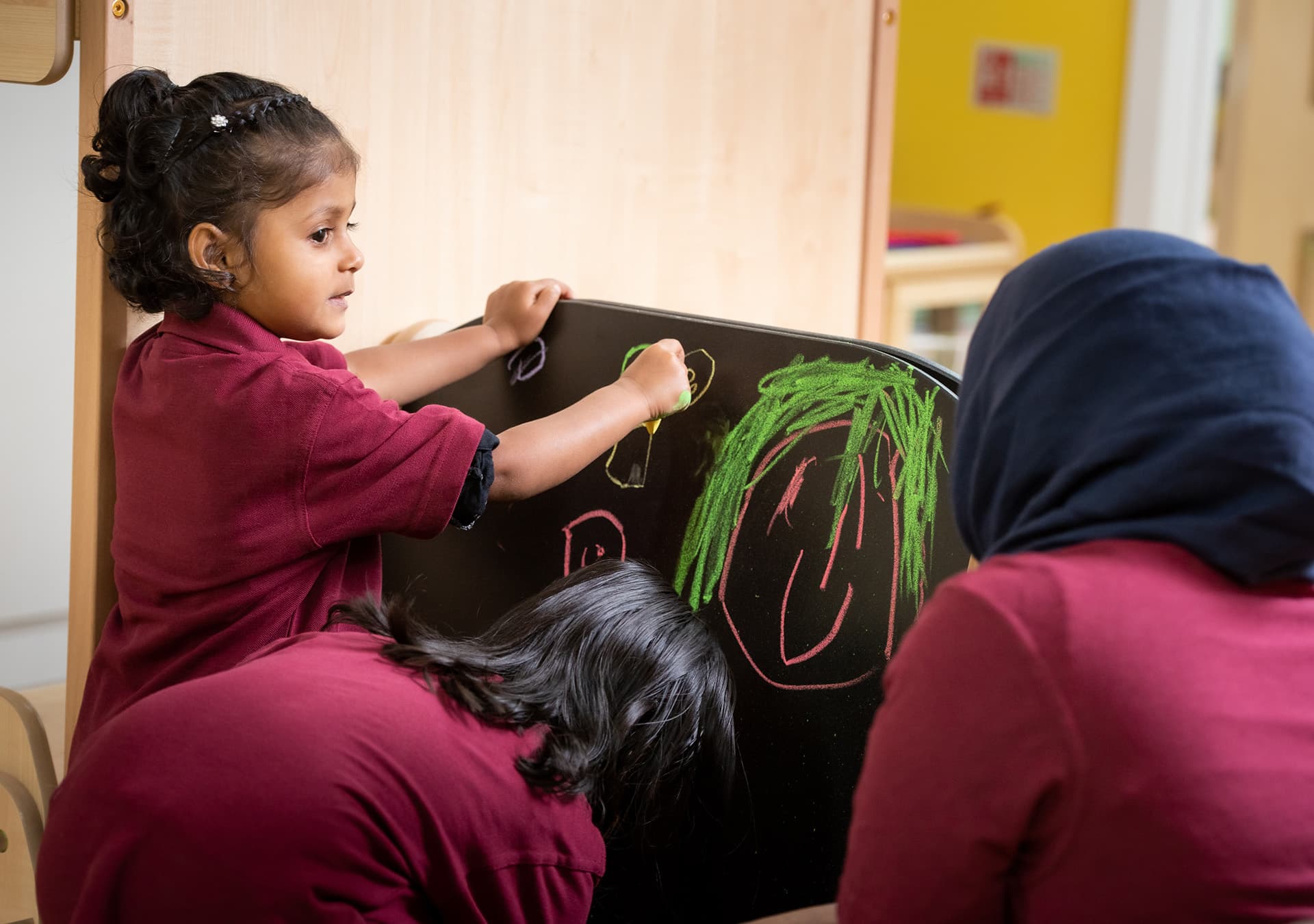 Girl drawing on a chalkboard with a staff member beside her