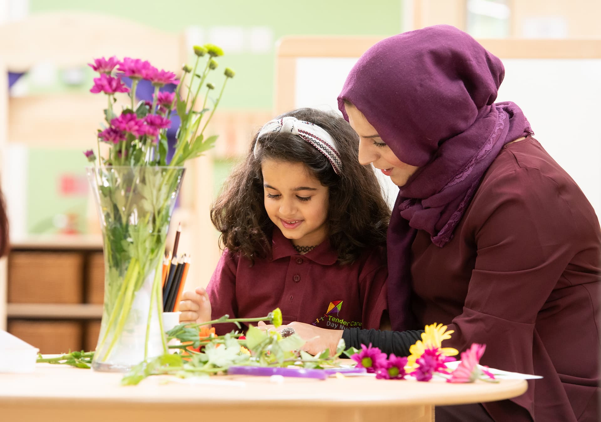 Girl and staff member arranging flowers and leaves at a table