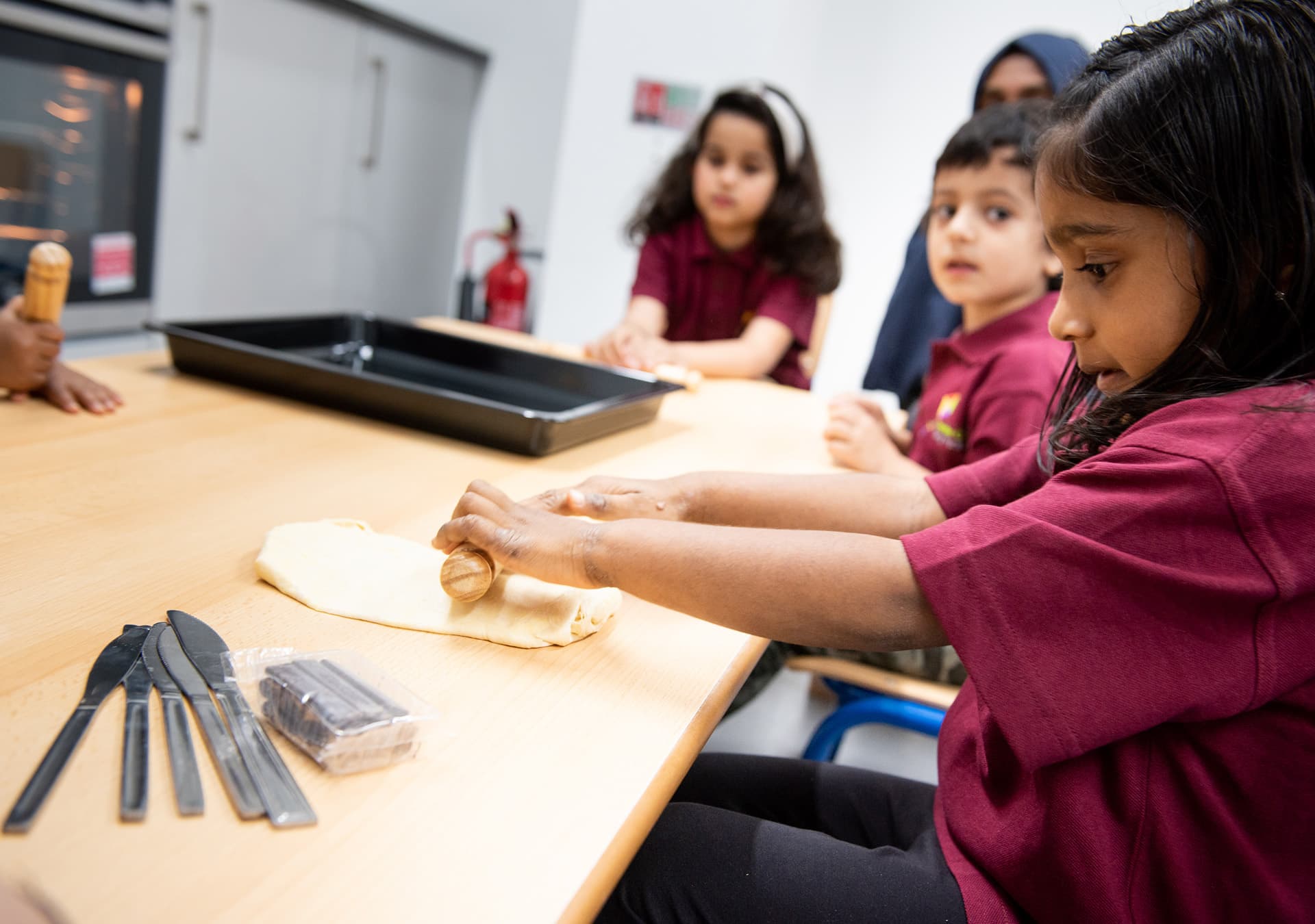 Children rolling out dough at a table with a staff member